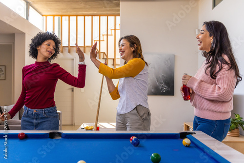 Konstfotografi Diverse female friends high-fiving around blue felt pool table in home, holding