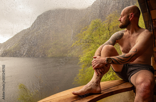 Man sitting in a sauna enjoying the view over the fjord