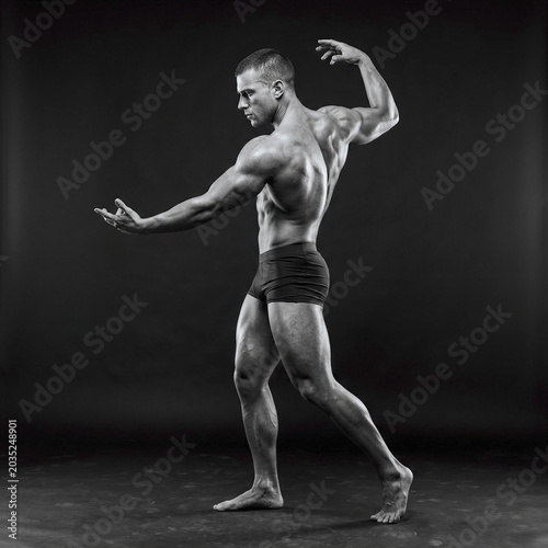 Muscular male athlete posing dynamically against dark studio backdrop with dramatic lighting