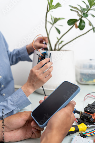 Young Asian woman and man using microcontroller and soil moisture sensors to measure soil moisture in a potted plant.