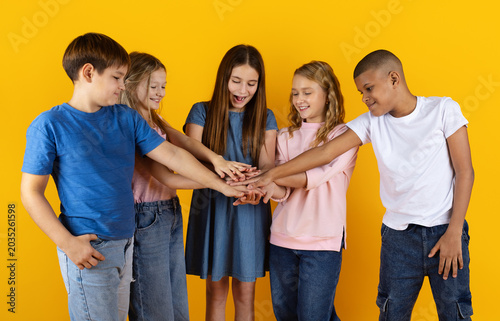 Photography School children stacking hands together on yellow studio background, symbolizing