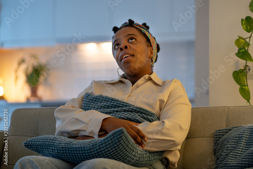 Bild auf Leinwand Irritated african american woman sits on sofa nervously looking upward after hearing disturbing noise from neighbors or apartment renovation
