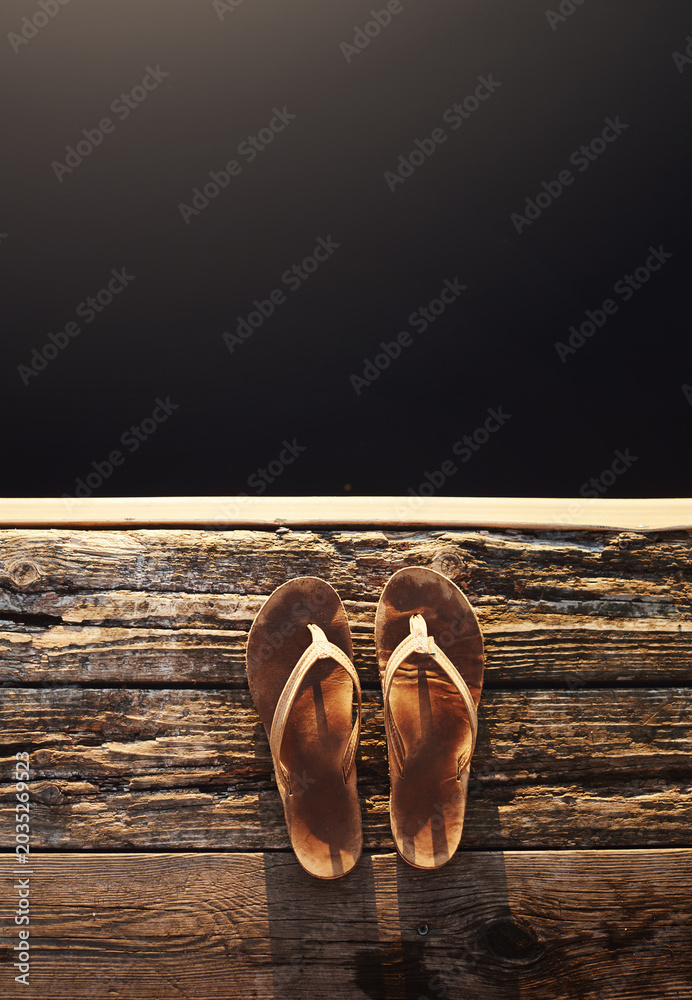 Obraz premium Sandals, black background and deck for travel, mockup space or holiday on vacation above. Wood jetty, flip flops and rustic pier for summer adventure, dark water and outdoor with top view of shoes