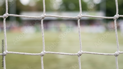 Close up selective focus of white soccer goal net with blurred football pitch background