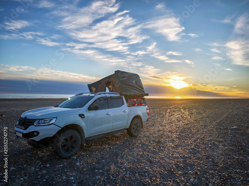 Overlanding 4x4 truck with rooftop tent on the beach at sunset.