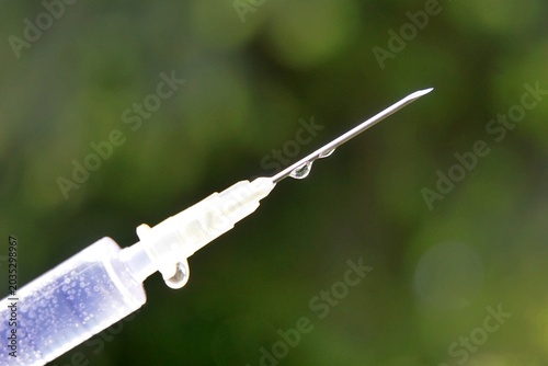 macro shot of a medical syringe needle pointed diagonally upward to the right against a soft, green background bokeh.