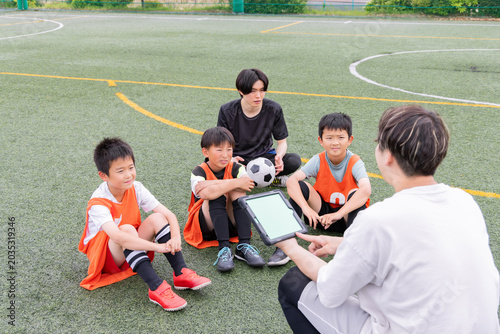 Photos タブレットを使って作戦説明をするサッカーコーチと少年選手たち