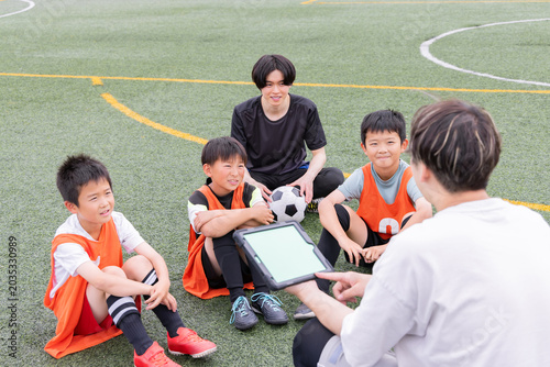 Photos タブレットを使って作戦説明をするサッカーコーチと少年選手たち