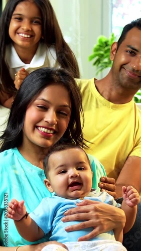 Indian parents and kids smiling while sitting together near sofa on floor in cozy modern living room, looking at camera indoors, enjoying bonding time, family connection, joy, and love at home