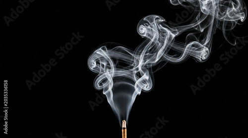 Delicate smoke swirls from incense stick against dark background, creating serene atmosphere
