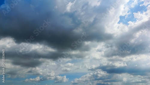 Slika na platnu The vast expanse of blue sky was filled with thick white and grey clouds that rolled quickly in the wind with the sun shining brightly behind the clouds