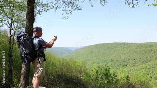 Middle-aged backpacker takes a cell phone snapshot of a scenic view from a mountaintop rocky outcrop vista