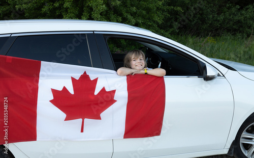 Canadian flag hangs on a car and a happy child looks out the window on Canada Day. Celebrate the national holiday