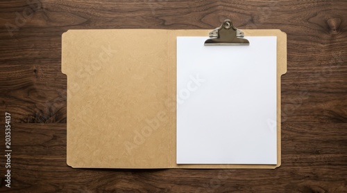 Open manila folder with clipboard and blank paper on dark wood desk top down view