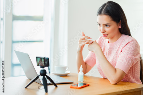 Young woman working with laptop computer in home kitchen. Work at home. Freelance, remote work. Woman advertises cosmetic products online