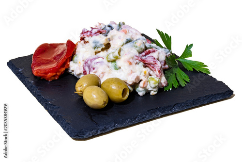 Valokuva Ensaladilla Rusa Casera, con hoja de perejil, olivas rellenas y pimientos del piquillo sobre una plato de pizarra negro