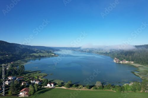 Lac jurassien vu par drone avec voile de brume et voilier solitaire