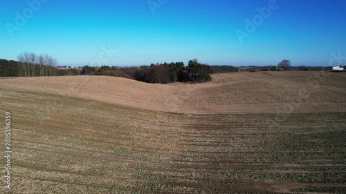 Backward drone flight over rolling fields and woodland grove