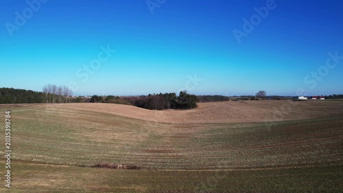 Forward drone flight over rolling farmland and woodland grove