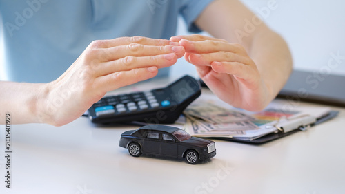Photos Hands shield a toy car above a calculator and cash