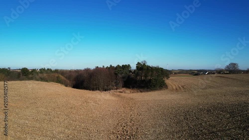 Forward drone flight over rolling farmland and woodland grove