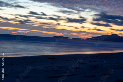 Serene tropical beach at dusk with calm ocean waters, colorful sunset skies, and distant coastal hills, perfect for travel blogs, tourism campaigns, vacation promotions, wallpapers, and relaxation.