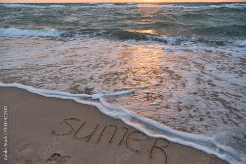 Sea water washing over text on sandy beach at dusk, minimal coastal landscape.