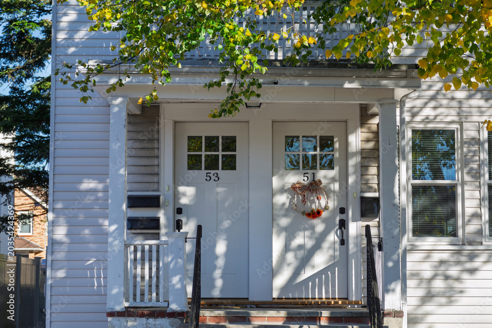 Naklejka premium White duplex house entrance with autumn wreath and dappled sunlight in Boston neighborhood 