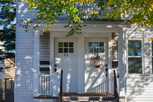 White duplex house entrance with autumn wreath and dappled sunlight in Boston neighborhood
