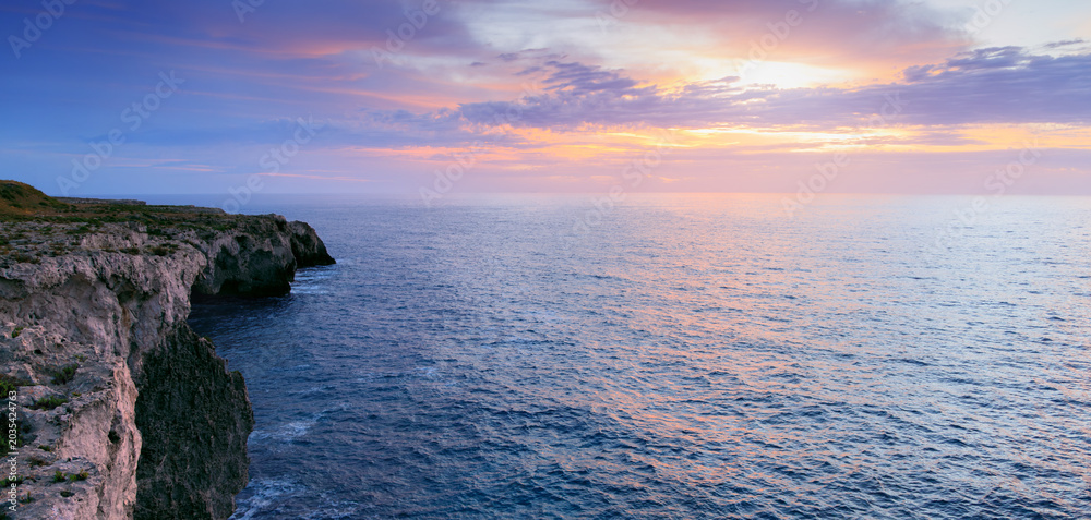Fototapeta premium Dramatic ocean cliffs meet a pastel sky at sunset with gentle waves below