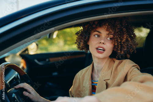 Tableau sur toile Cheerful woman driving car, looking aside, sunlit interior moment, casual jacket