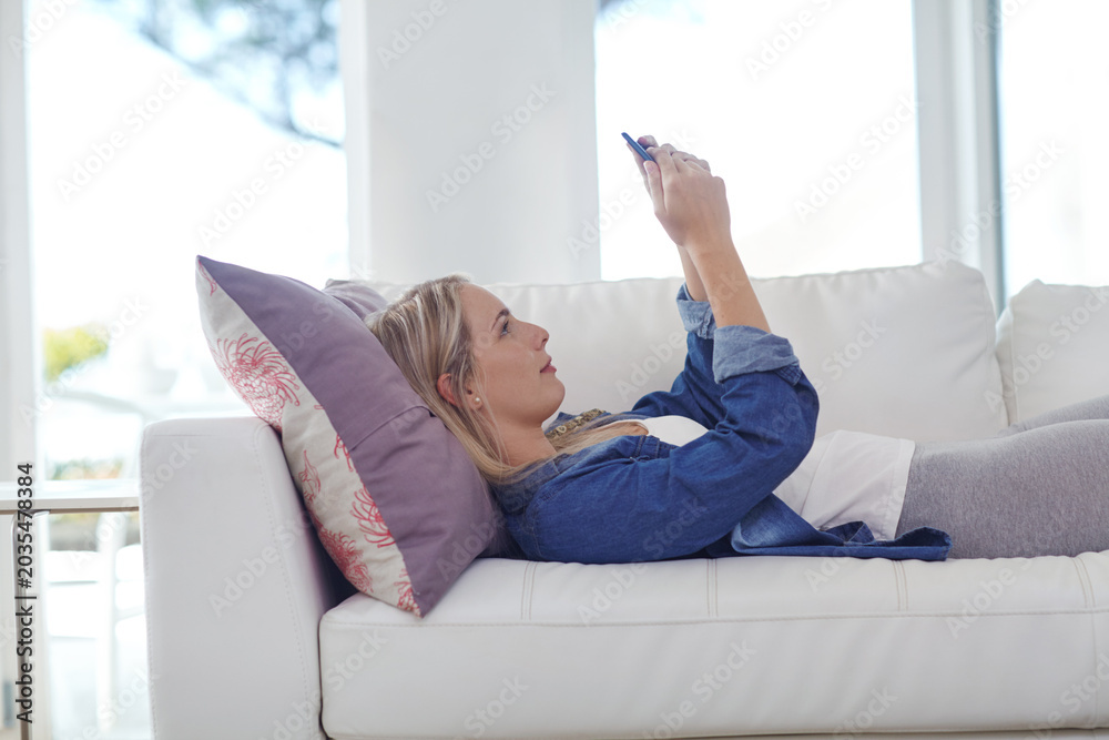 Fototapeta premium Woman, phone and relax on couch, texting and happy with notification for online dating at apartment. Girl, smartphone and lay on sofa with mobile app, scroll or web chat on social network at house