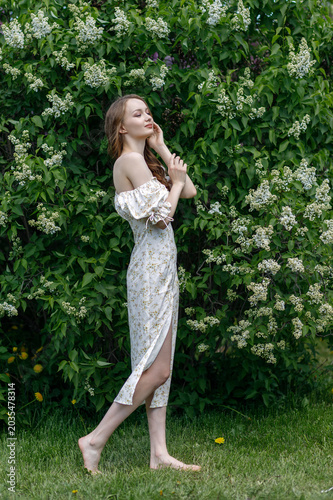 Canvastavla Portrait of a young woman with long hair in a white dress among blooming lilacs