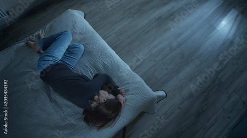 Top view of lonely woman lying in fetal position on bed during night. Depressed female suffering from insomnia or psychological trauma inside dark bedroom.