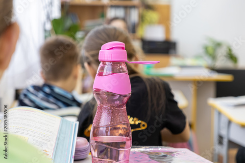 Pink reusable water bottle on a desk in an elementary school classroom, encouraging hydration habits and healthy lifestyle choices for students during their daily lessons at school