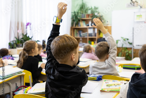 Students raising hands in a primary school classroom to answer a teacher question, representing active learning, student engagement, and educational participation in the school system