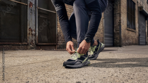 Man tying his shoelaces on an urban sidewalk, athlete preparing for a run wearing streetwear-inspired running shoes and activewear, lifestyle concept.