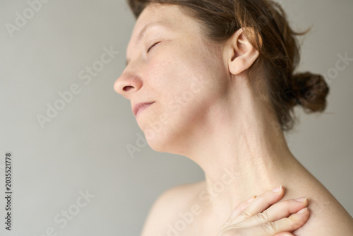 Tableau sur toile Woman Tilting Head Eyes Closed Touching Shoulder In Soft Indoor Light With Neutral Background Bare Shoulders And Relaxed Pose Implying Self Care Or Contemplation