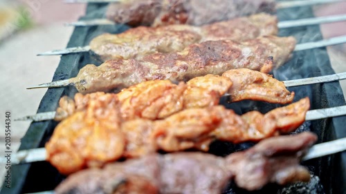 Close up of shashlik on metal skewers made from different kinds of meat cooking on hot brazier with smoke. Outdoor barbecue scene with selective focus.