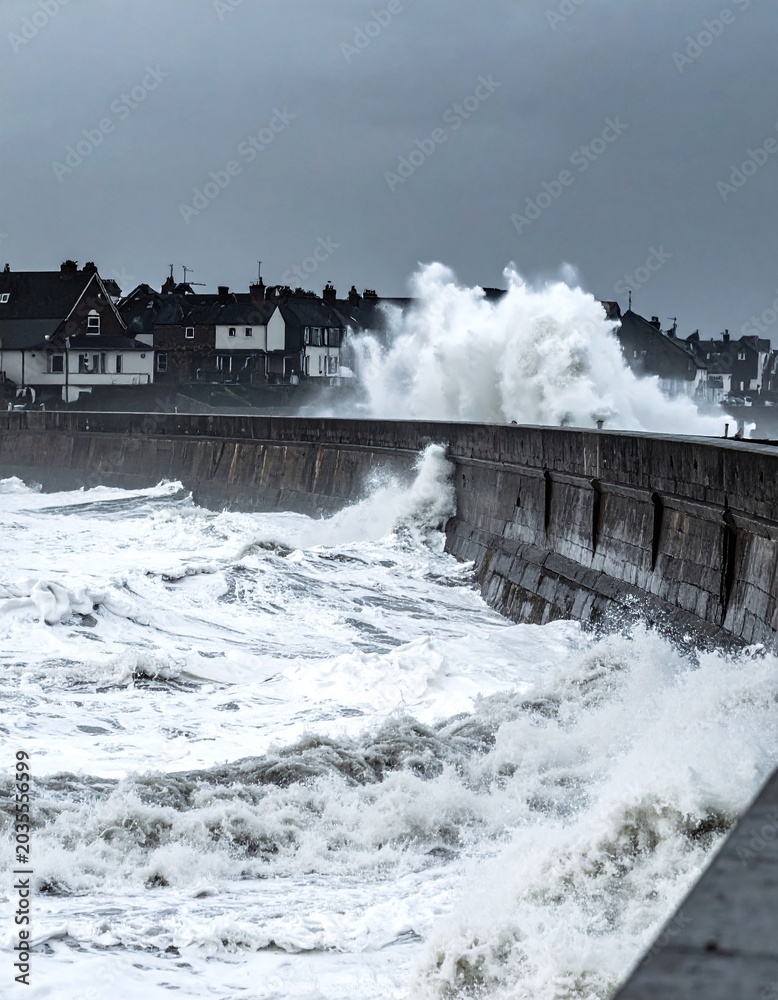 Obraz premium Powerful ocean waves crash against a stone sea wall during a dramatic storm. This moody coastal scene captures raw natural force and resilience, perfect for environmental or news media.