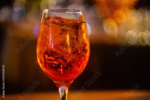 An aperol spritz drink on a glass at a lively bar during the evening with defocused background