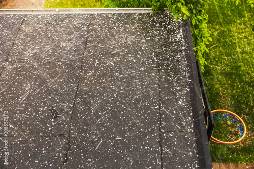 Close up view of severe hailstorm hitting dark rooftop during heavy rain near green trees. Sweden.