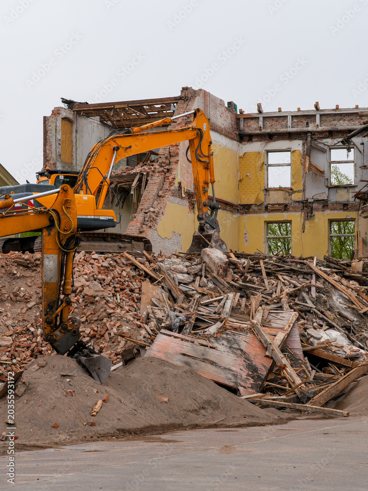 Fototapeta premium Excavator demolishing abandoned brick building with rubble and timber debris at construction site