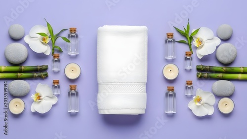A serene spa setting with a neatly folded white towel at its center, surrounded by smooth stones, delicate orchid blossoms, bamboo stalks, small bottles of essential oil, and lit candles.