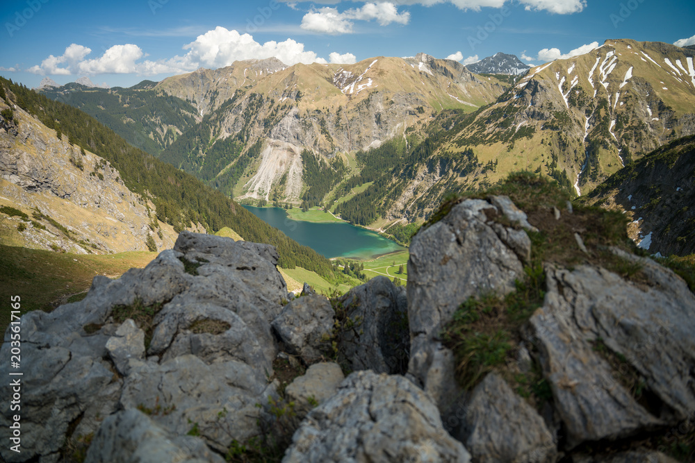 Obraz premium Alpine Lake and Mountain Valley Framed by Rocky Foreground Under Blue Sky