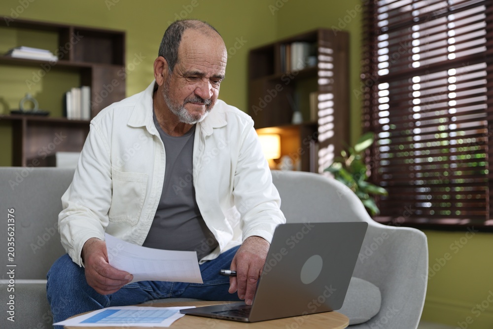 Obraz premium Pension. Senior man with laptop and paperwork at table indoors. Space for text