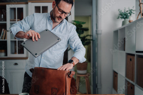 Photography Man packing laptop into shoulder bag, preparing to leave home office for a remot