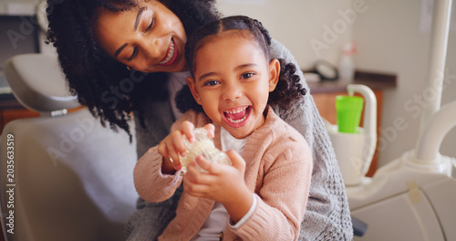 Happy child  mother and tooth model at dentist office for learning oral health  play and excited. Mom  girl and pediatric orthodontics with teeth  typodont and dental care with parent for portrait