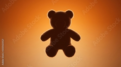 Minimalist composition featuring a brown teddy bear silhouette against a warm orange gradient background. The bear is seen from
