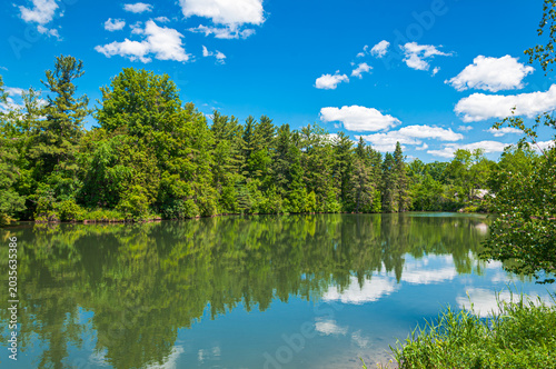 Beautiful tranquil sunrise landscape with a calm lake reflecting green forest trees and colorful clouds in Ontario, Canada. A peaceful nature scene.